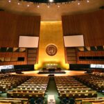 Wide interior view of the United Nations General Assembly hall with rows of seats and a speaker's podium