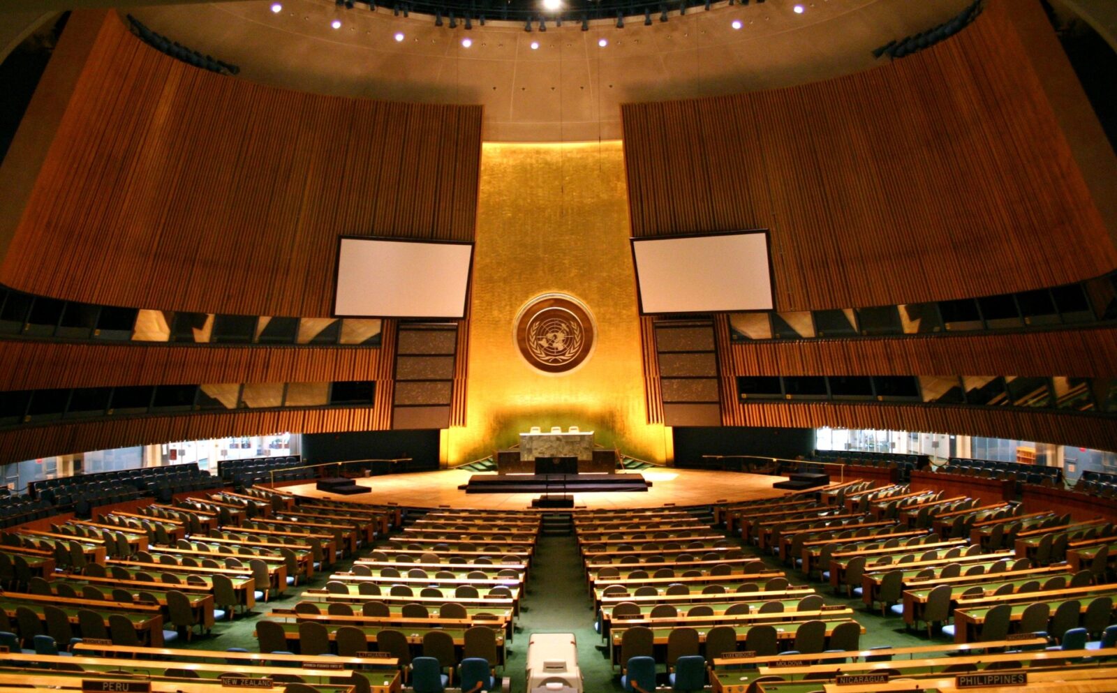 Wide interior view of the United Nations General Assembly hall with rows of seats and a speaker's podium