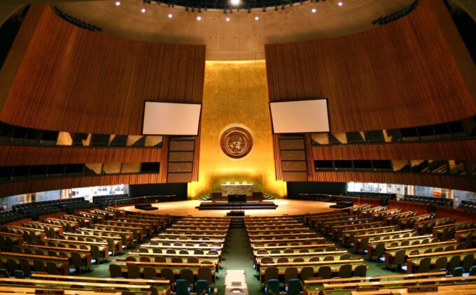 Wide interior view of the United Nations General Assembly hall with rows of seats and a speaker's podium