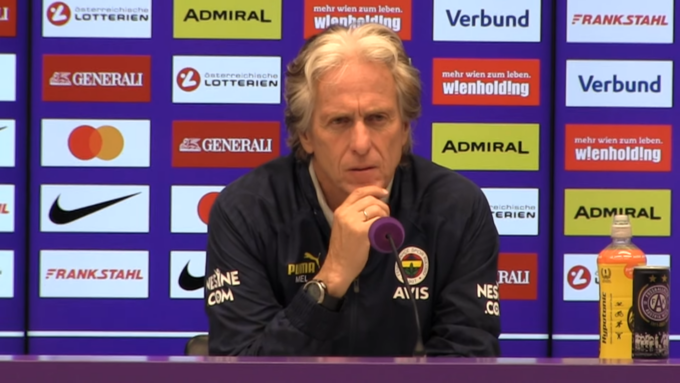 Jorge Jesus speaking at a press conference, standing in front of microphones and a backdrop